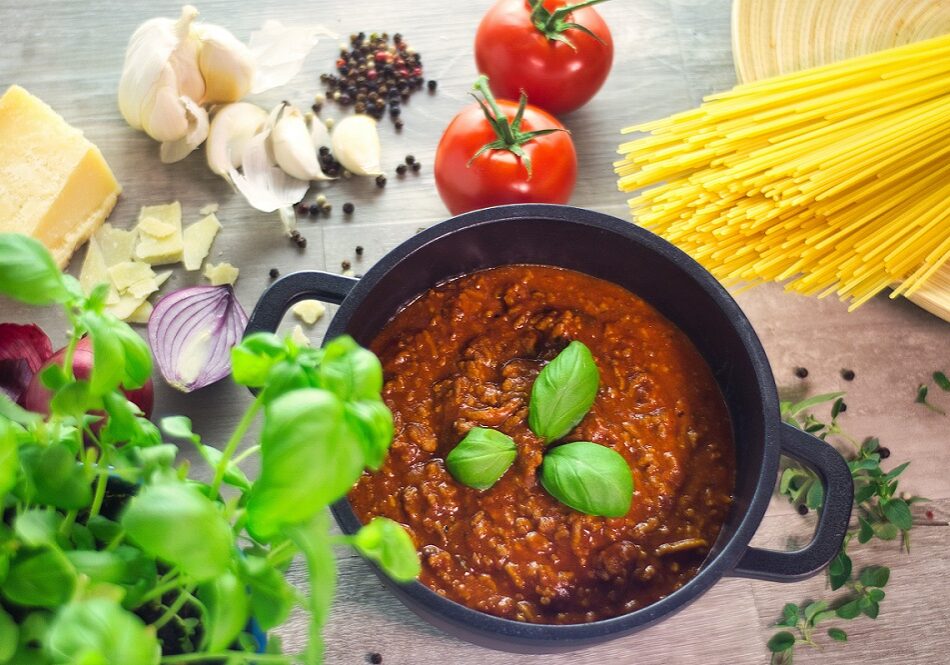Homemade sauce bolognese in a black iron pot with ingredients on a wooden table